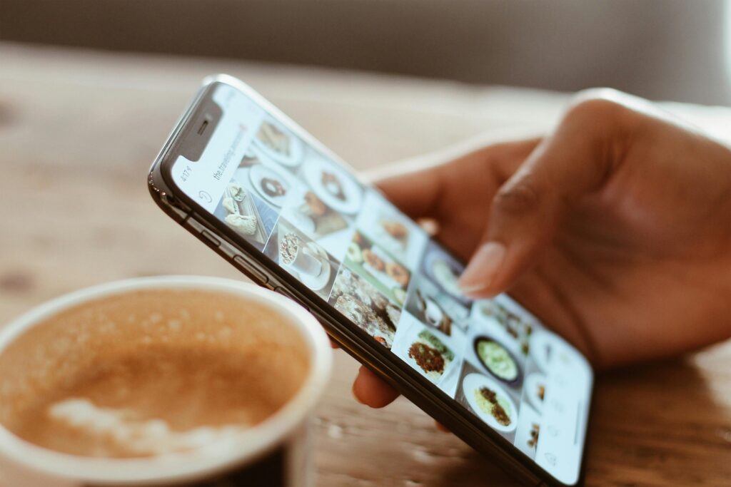 Hand browsing social media photos on a smartphone next to a cup of coffee indoors.