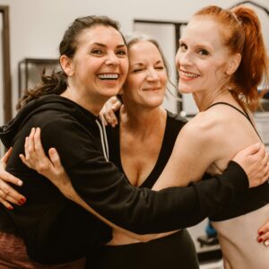 Three happy women hugging at the gym, celebrating friendship and wellness.