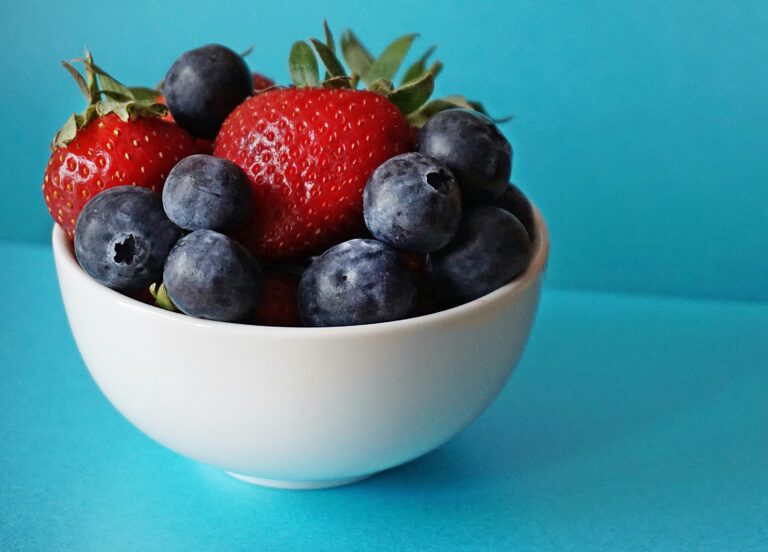 A vibrant mix of fresh strawberries and blueberries in a white bowl on a blue background.